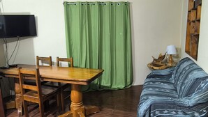 Een kamer met een houten eettafel, stoelen, een groen gordijn, een bank, een lamp en een televisie.