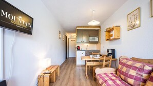 En kompakt opholdsstue med et tekøkken, spiseplads og sofa.