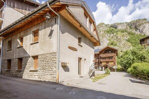 Ein traditionelles Chalet mit Steinwänden und hölzernen Balkonen, eingebettet in eine Berglandschaft mit blauem Himmel.