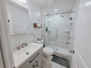Ein modernes Badezimmer mit einem weißen Marmorwaschbecken, einer Toilette und einer Duschkabine.