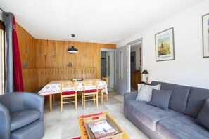 A living room with a grey sofa, a dining table with chairs, and a wooden wall panel.
