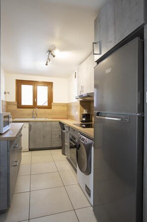 A compact kitchen with a built-in washer and dryer, a stainless steel refrigerator, and a window above the sink.