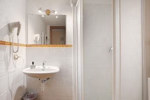 A bathroom with a sink, mirror, hairdryer, and shower.