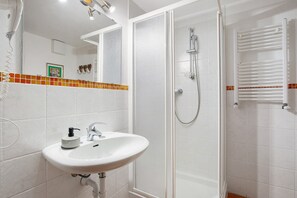 Une salle de bain avec un lavabo blanc, une douche dotée d’une porte en verre et un porte-serviettes.
