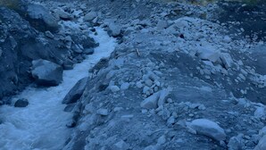 Un paysage montagneux accidenté, avec un cours d’eau rocheux, des sommets enneigés et un ciel dégagé.