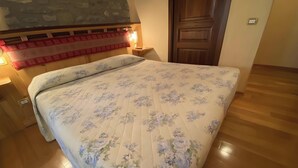 Une chambre à coucher avec une couvre-lit à motifs floraux, un plancher en bois, une tête de lit en bois, une table de chevet avec une lampe et une porte.
