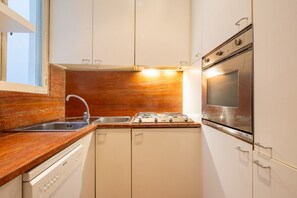 A compact kitchen with white cabinets, a stainless steel sink, a gas stove, and a built-in oven.