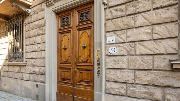 Uma porta dupla de madeira com puxador de latão, em um edifício de pedra com uma placa numérica '44' na parede.