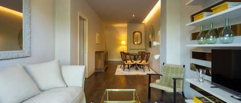 A modern living room with a sofa, a coffee table, a dining area with chairs, and a bookshelf with decorative items.