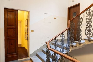 A staircase with ornate metal railings and a wooden handrail, leading to a room with a wooden door and a framed picture on the wall.