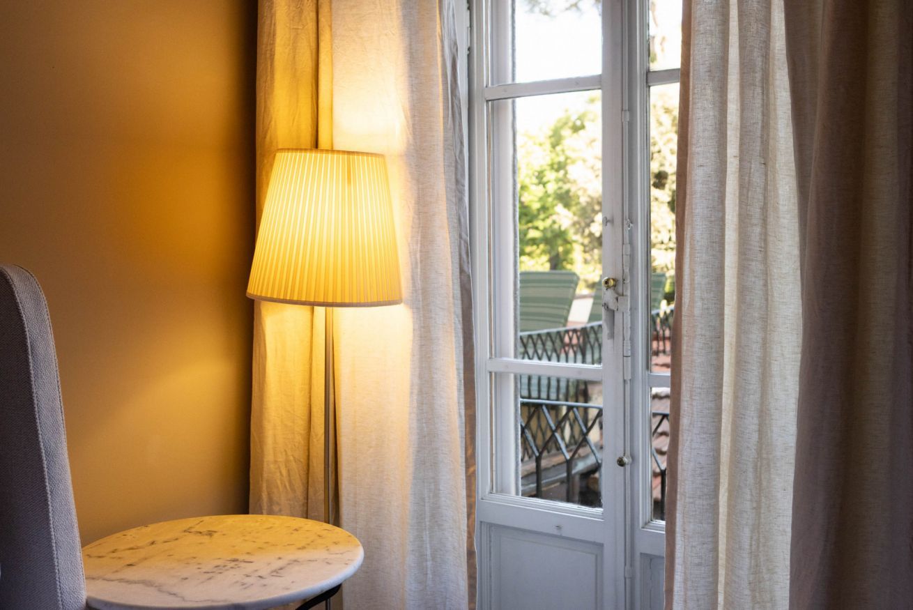 A room with a round table, a lamp, and a door leading to an outdoor area with a railing.
