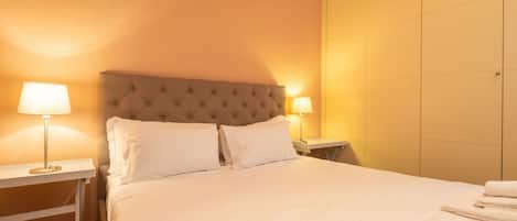 A hotel room with a large bed, two bedside lamps, and a nightstand.