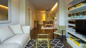 Uma sala de estar moderna com sofá, mesa de centro, área de jantar com cadeiras e estante com objetos decorativos.