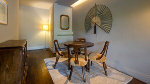 Un comedor con una mesa redonda y seis sillas, un aparador de madera, una lámpara de pie y un ventilador fijado a la pared.