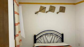 Un dormitori petit i ordenat amb un llit individual, una taula petita i una porta.