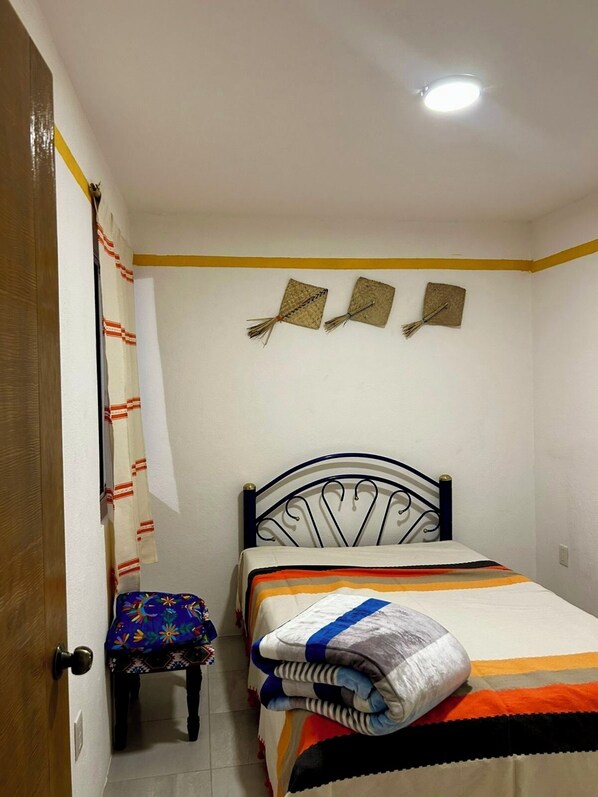 A small, neatly arranged bedroom with a single bed, a small table, and a door.