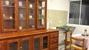 A room with a wooden cabinet with glass doors, a dining table with chairs, and a window.