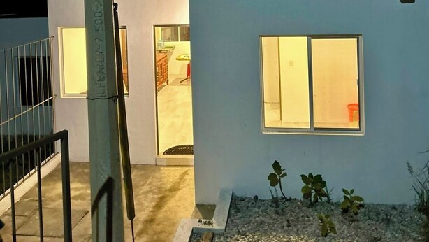 A modern building with two illuminated windows, a metal railing, and a gravel area with plants.
