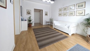 Un vaste espace de vie agrémenté d’un canapé blanc, d’un parquet, d’un grand tapis et de plusieurs tableaux encadrés accrochés aux murs.
