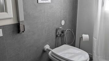 A modern bathroom with a toilet, bidet, and a trash bin.