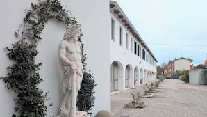 Un bâtiment blanc surmonté d’une statue d’un homme, placée sur un piédestal, et entouré de verdure.