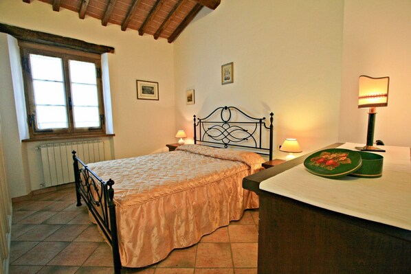 A bedroom with a bed, a nightstand, a lamp, a radiator, and a window.