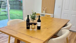 A wooden dining table with three wine bottles and glasses, surrounded by chairs. - Modern Home w/ Theater, BBQ & Private Yard (Ladson)
