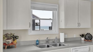 A kitchen with a window, a sink, cabinets, and a dishwasher. - Mid-Century Modern! Steps to Beach/Pool. NEW Remodel, Ocean Views from 4  Decks! (North Topsail Beach)