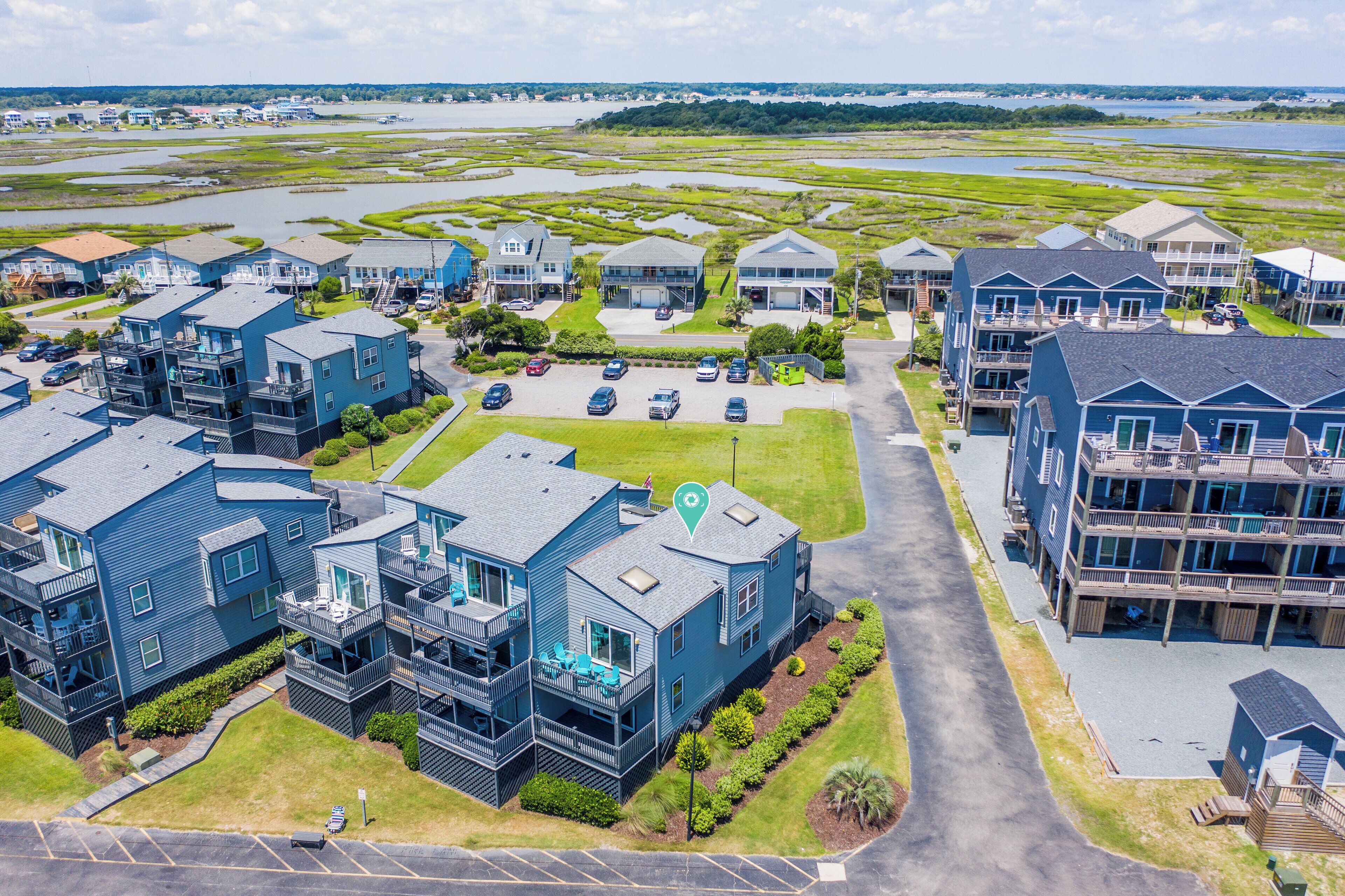 A residential area with multiple two-story houses, a parking lot, and a view of a large body of water in the background.