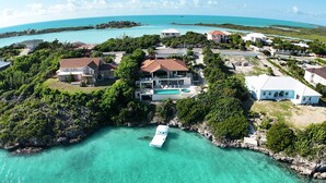 Vue aérienne d’une propriété située sur la côte, avec une grande maison, une piscine et un bateau amarré près de l’eau.