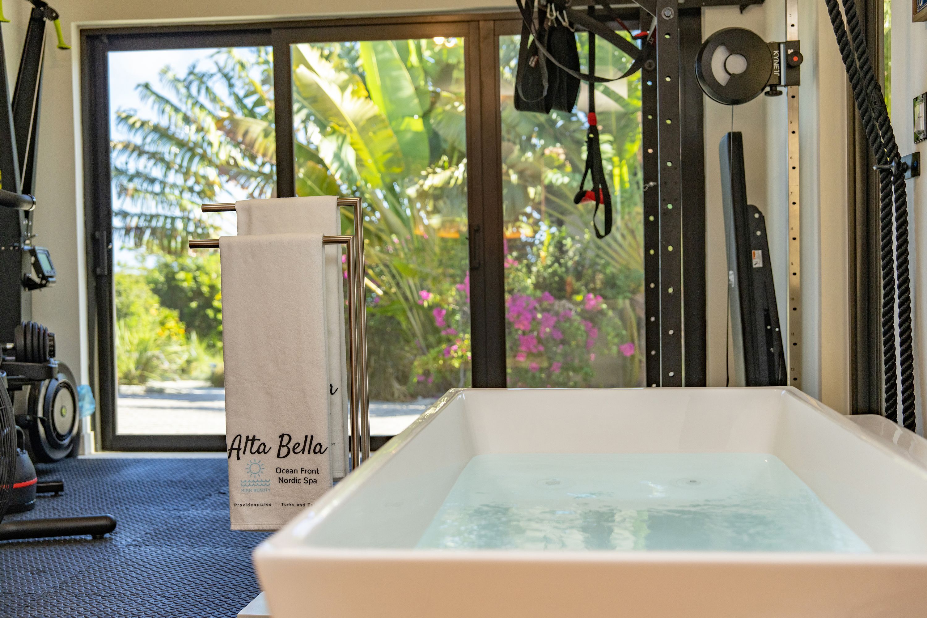 Ein Spa-Raum mit Badewanne, Fitnessgeräten und Blick auf tropische Vegetation.