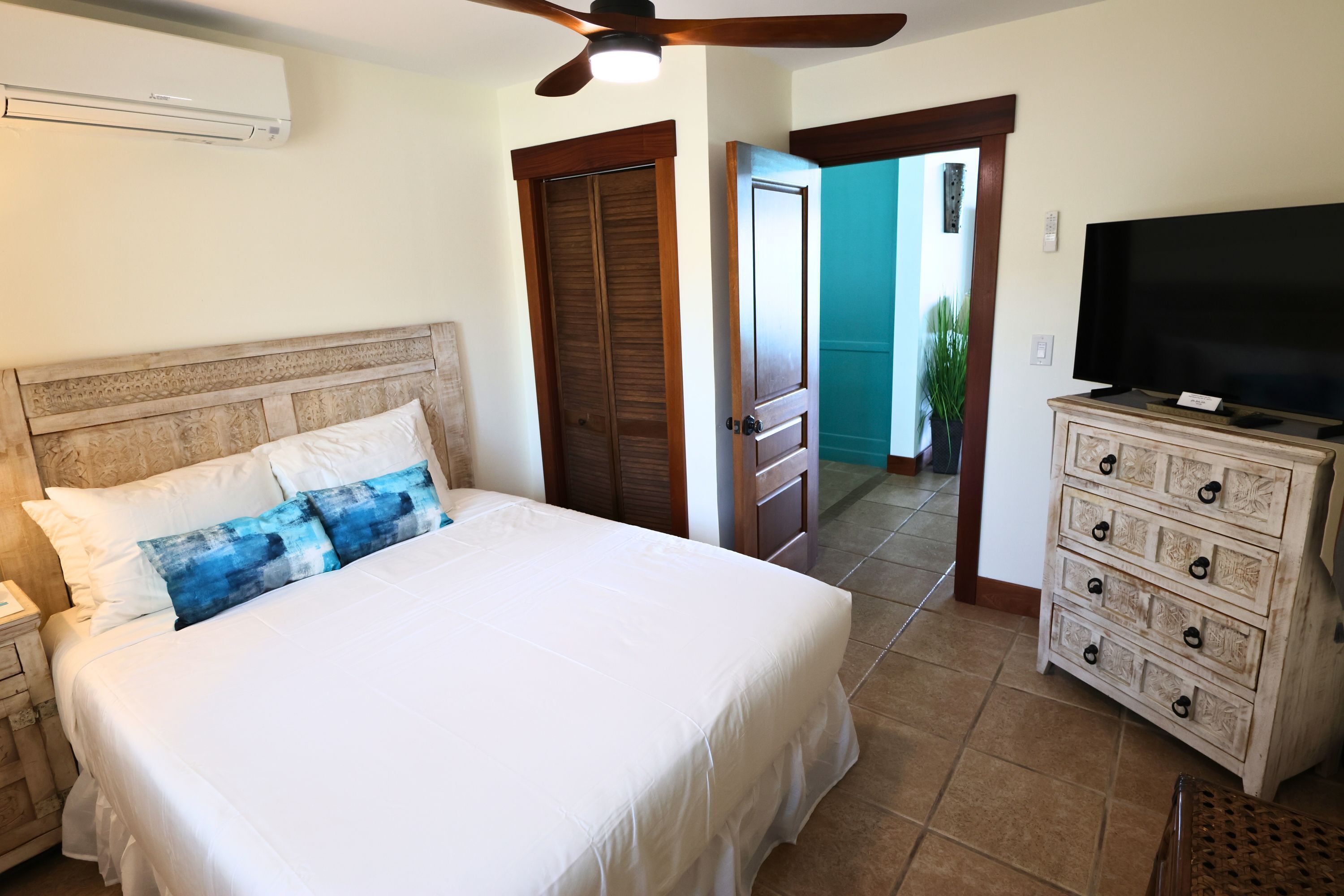 Une chambre à coucher avec un lit, une commode, un téléviseur et un ventilateur de plafond.