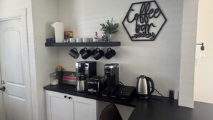 Una cocina con cafetera, tostadora, hervidor y tazas sobre la encimera.