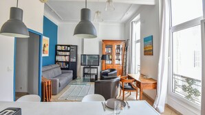 Ein modernes Wohnzimmer mit einem grauen Sofa, einem Holzschrank und einem Essbereich mit Tisch für zwei Personen.