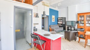 Ein modernes Wohnzimmer mit roter Akzentwand, einem grauen Sofa, einer Holzhütte mit Büchern und einem Fernseher.
