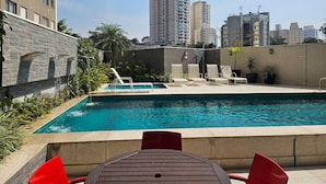 Piscina no terraço com espreguiçadeiras, cercada por edifícios altos.