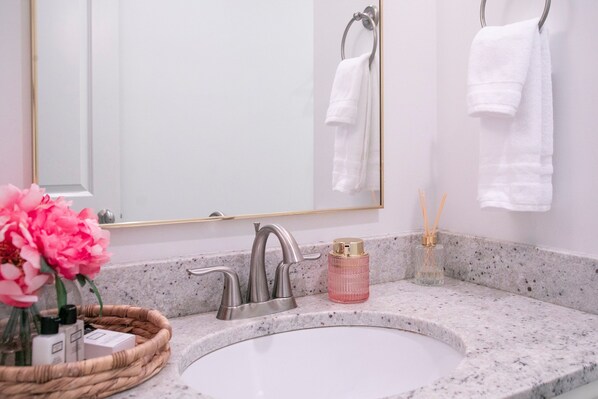 A bathroom with a white sink, a large mirror, and two white towels hanging on hooks.