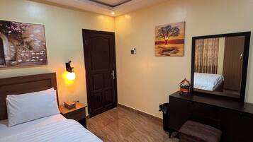 A hotel room with a bed, a desk, a chair, a dresser, a mirror, a ceiling fan, and artwork on the walls.