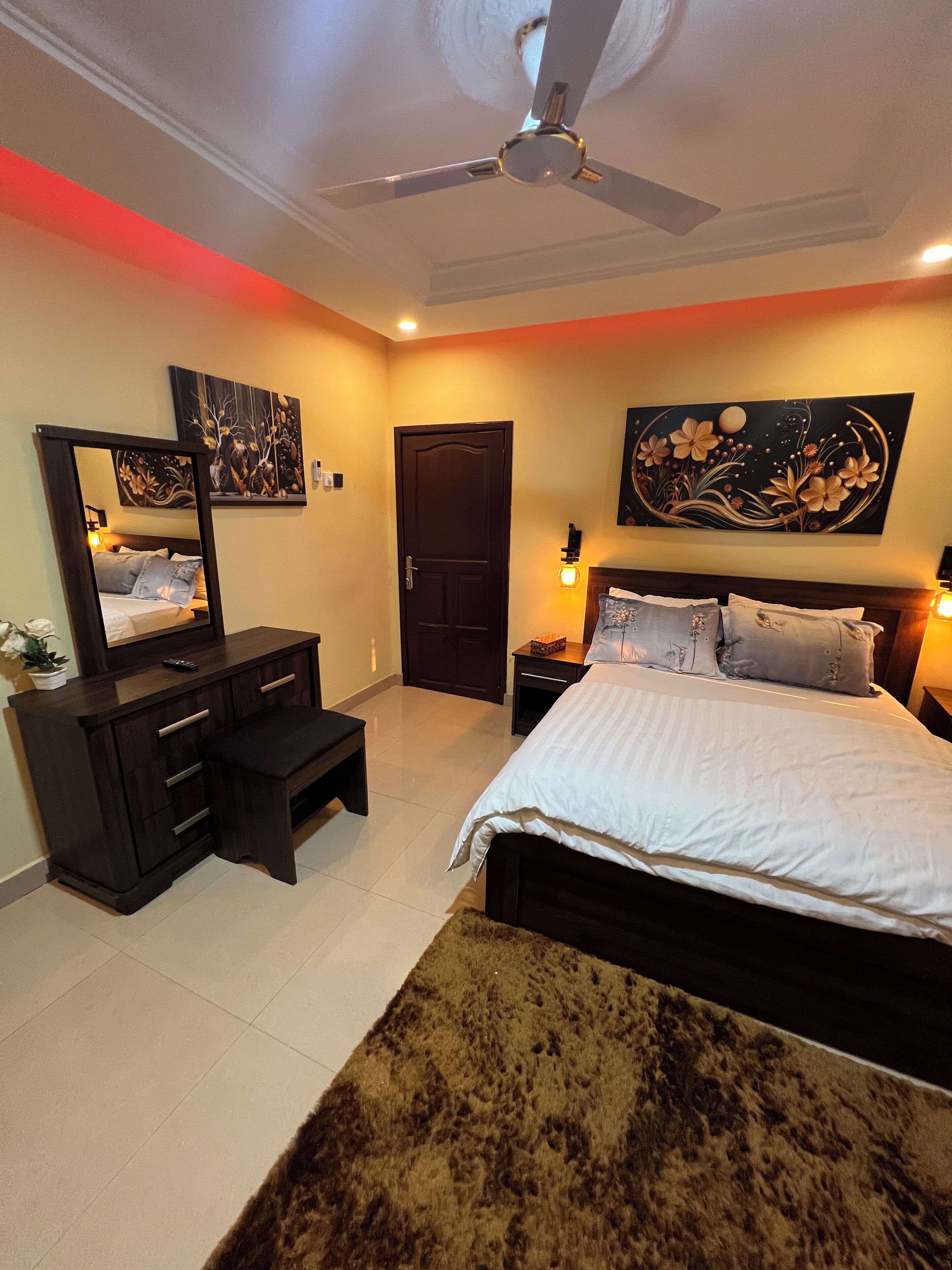 A bedroom with a bed, a dresser, a mirror, a ceiling fan, and artwork on the walls.