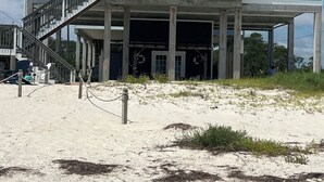 Ein zweistöckiges Strandhaus mit Balkon, Treppe und einem Sandstrand davor.