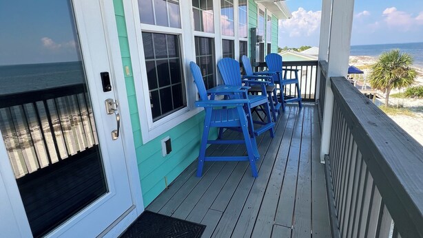 Eine überdachte Veranda mit Blick auf den Ozean, mit einer Tür mit Fenster, einem blauen Stuhlgarnitur und einem kleinen Tisch.