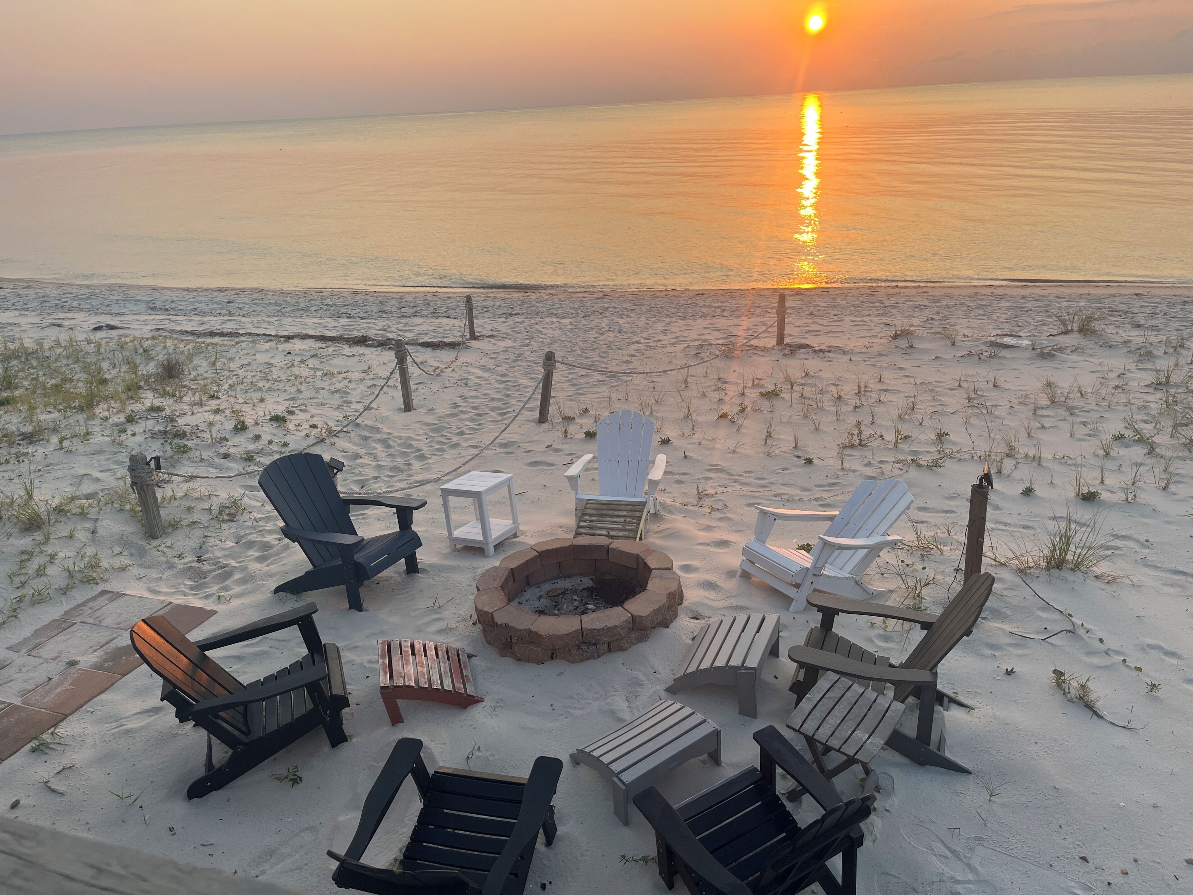A beachside seating area with Adirondack chairs and a fire pit, overlooking the ocean.