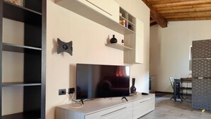 A modern living room with a flat-screen TV mounted on a wooden cabinet, a built-in shelf unit, and a dining area with a table and chairs.