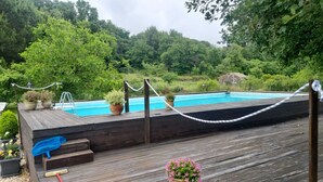 A wooden deck with a pool, surrounded by lush greenery and trees.