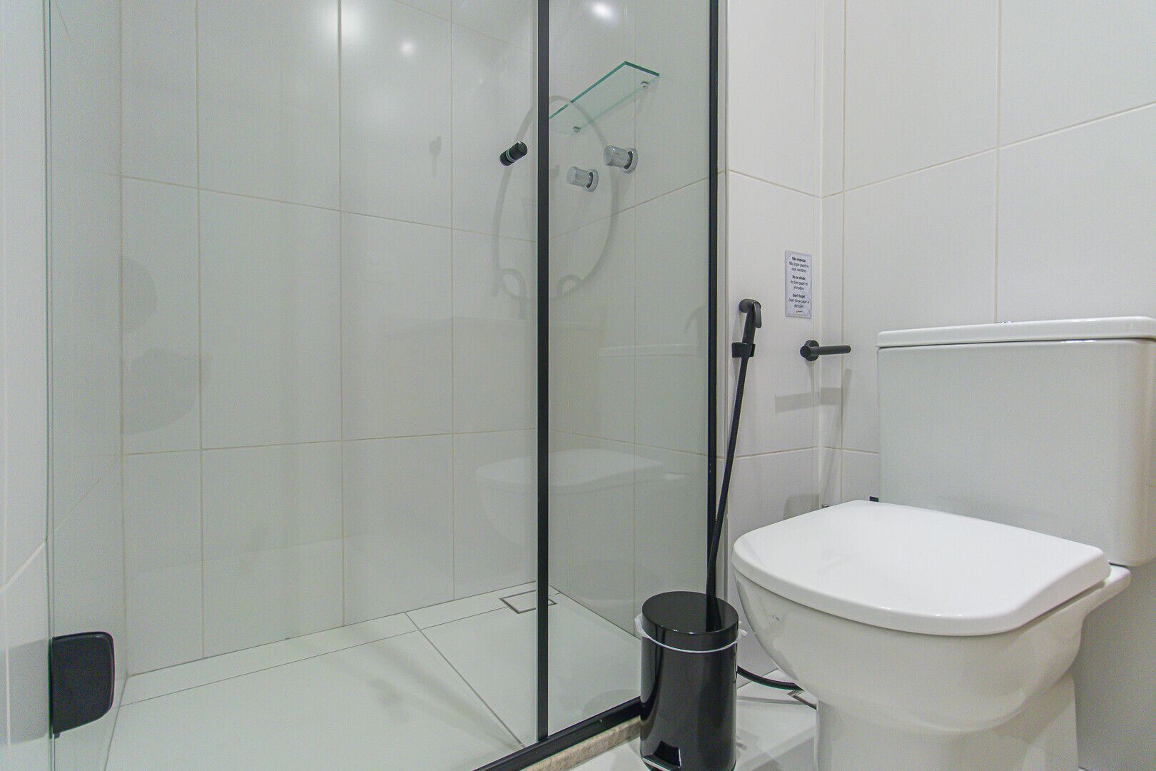 A modern bathroom with a glass-enclosed shower, a white toilet, and a glass shelf.
