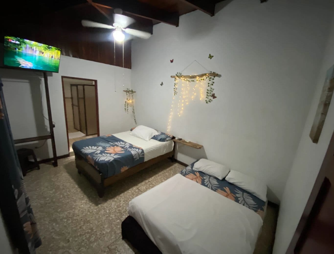 A bedroom with two beds, a ceiling fan, a TV, and decorative lights.