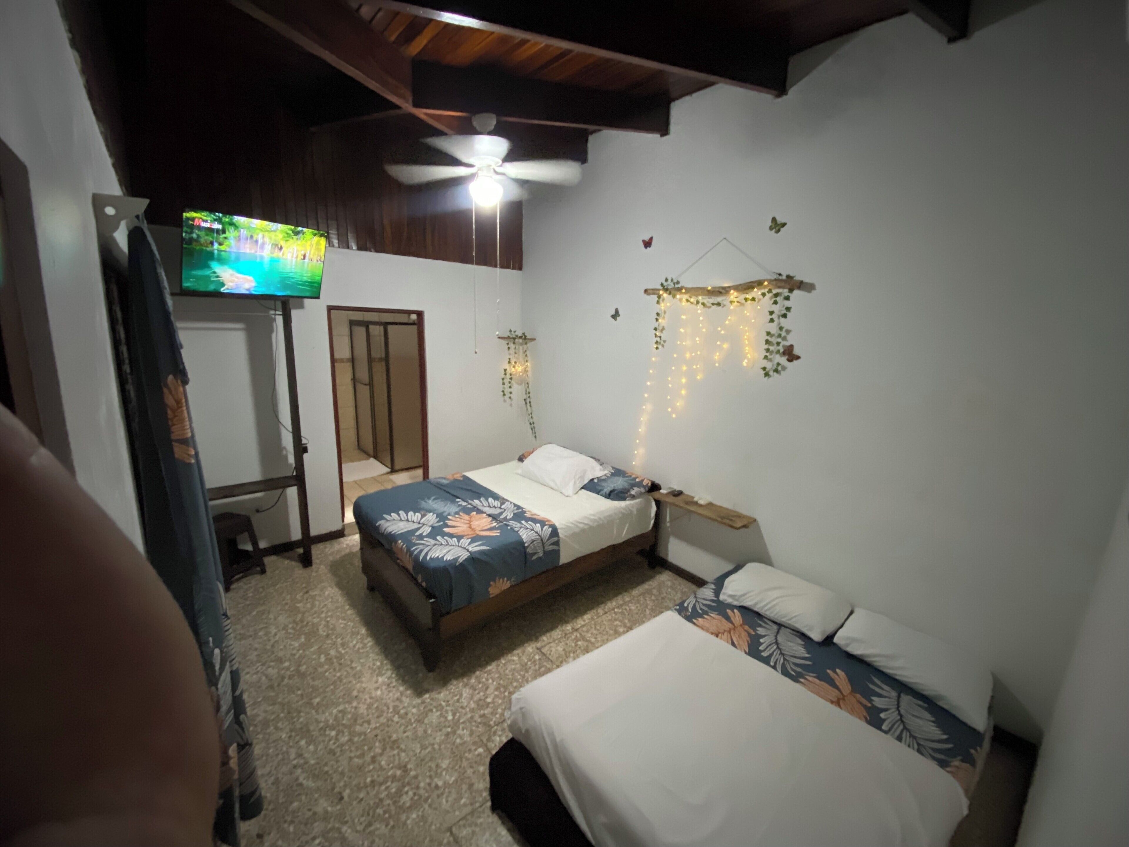 Un dormitorio con dos camas, ventilador de techo, televisor y un adorno en la pared.