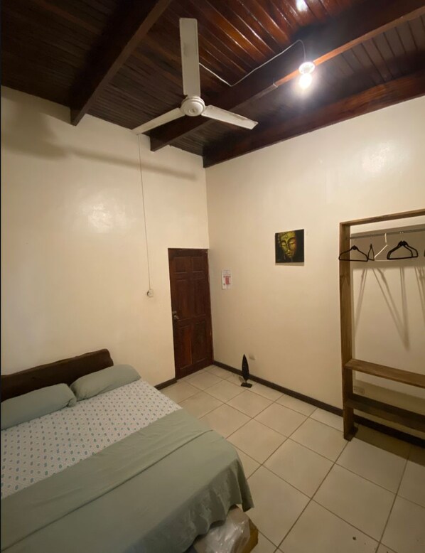 Un dormitorio con cama, ventilador de techo, puerta de madera y perchero en la pared.