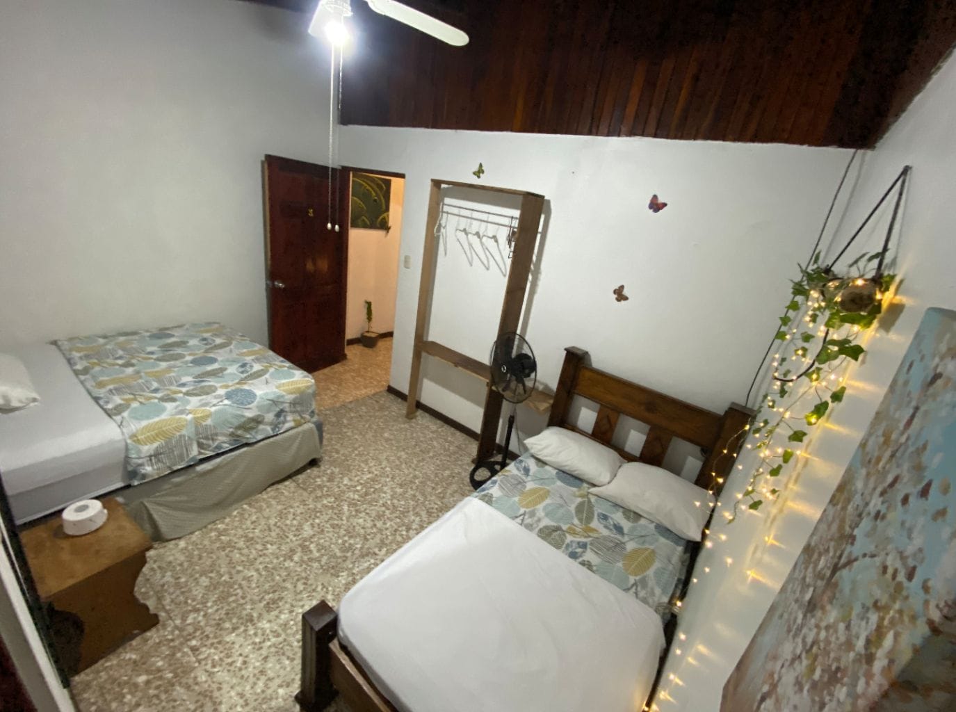 A bedroom with two beds, a wooden ceiling, a door, and a fan.