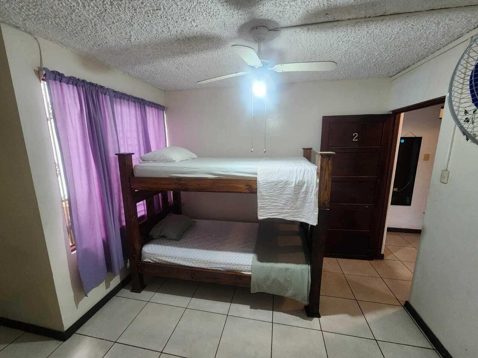Ein Schlafsaalzimmer mit Etagenbetten, einem Deckenventilator und einer Tür mit einer Nummer.